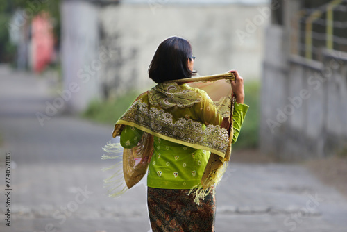 Javanese woman wearing traditional Kebaya dress walking alone on a village alley photo