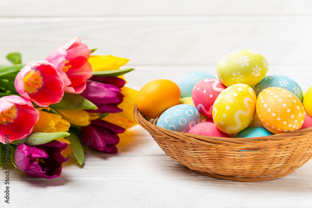 Easter basket filled with colorful eggs and a bouquet of tulips on a textured wooden table. Easter celebration concept. Colorful easter handmade decorated Easter eggs. Place for text. Copy space Easter basket filled with colorful eggs and a bouquet of tulips on a textured wooden table. Easter celebration concept. Colorful easter handmade decorated Easter eggs. Place for text. Copy space
