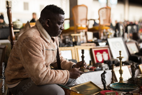 ordinary Afro-American guy considers things sacond hands on flea market photo