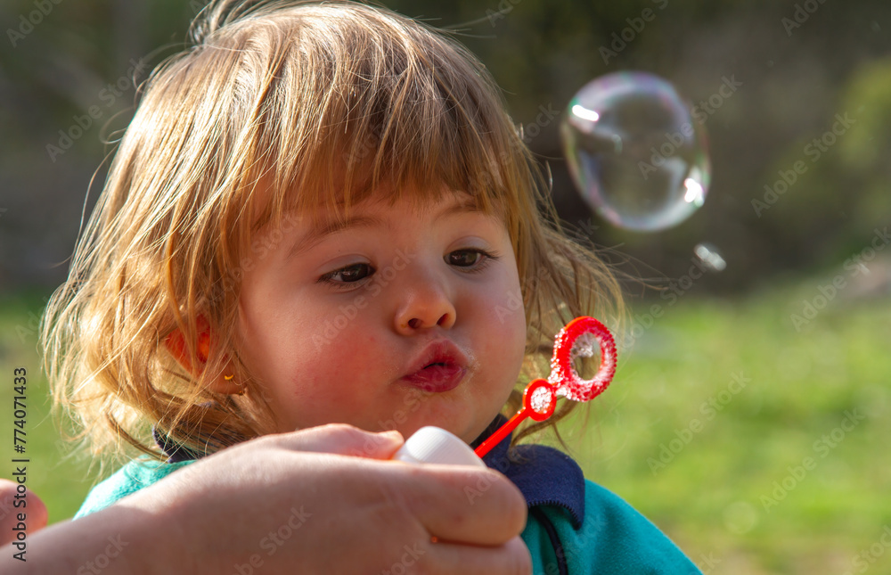 A pretty two-year-old blonde girl plays with blowing soap bubbles on a sunny day
A pretty two-year-old blonde girl plays with blowing soap bubbles on a sunny day