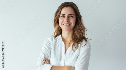An ambitious and confident woman in her 30s stands before a white background, holding her arms across her chest and smiling big at the camera.