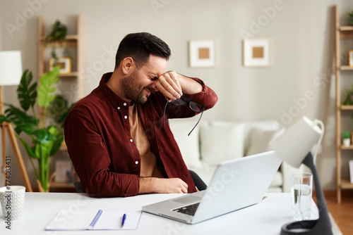 Young man has a headache while working in the office at a table with a laptop