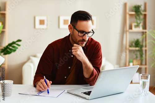 Young business man working at home with laptop and papers on desk.