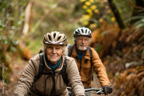 A senior couple wearing helmets, riding bikes through a dense forest surrounded by tall trees and greenery © Ilia Nesolenyi