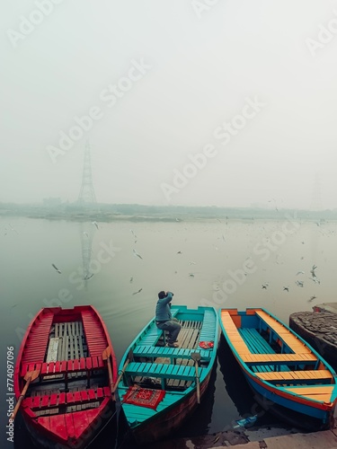 Photography Vertical shot of colorful boats and seagulls flying over them and the river in Delhi, India