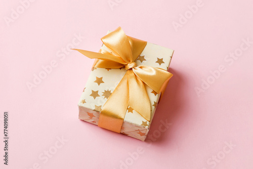 wrapped Christmas or other holiday handmade present in white paper with gold ribbon on colored background. Present box, decoration of gift on colored table, top view with copy space