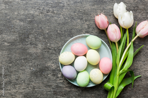 Happy Easter composition. Easter eggs in basket on colored table with yellow Tulips. Natural dyed colorful eggs background top view with copy space