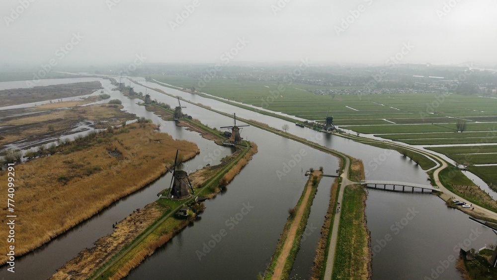 Aerial shot of the Windmills at Kinderdijk and a bridge on a river in a foggy weather
