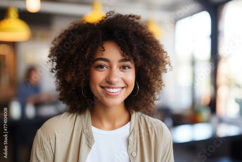 Close-up of a pretty African american teenage lady with curly hair is smiling and wearing a tan jacket and white shirt. She is posing for a picture in a restaurant © Sascha