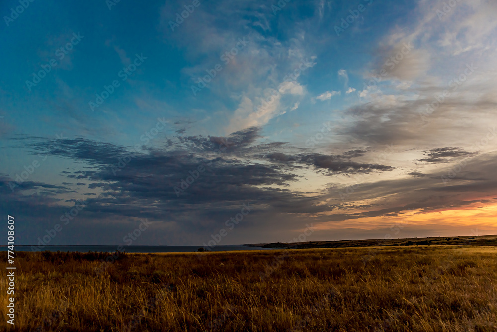 Sunrise or sunset in the Russian steppe at golden hour. Stratus, Cirrocumulus and Altocumulus clouds. The sun is shining from behind a cloud. Red orange and white shades. Morning or evening.