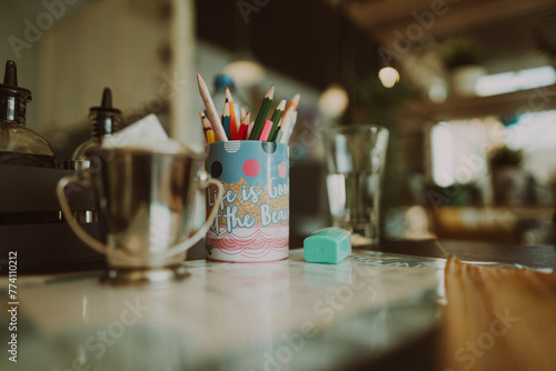 Metal pen box full of colorful pencils placed in a kitchen full of tools for making drinks