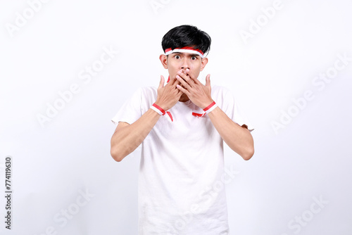 Shocked Young asian boy with red white ribbon celebrating Indonesia independence day while covering his mouth photo