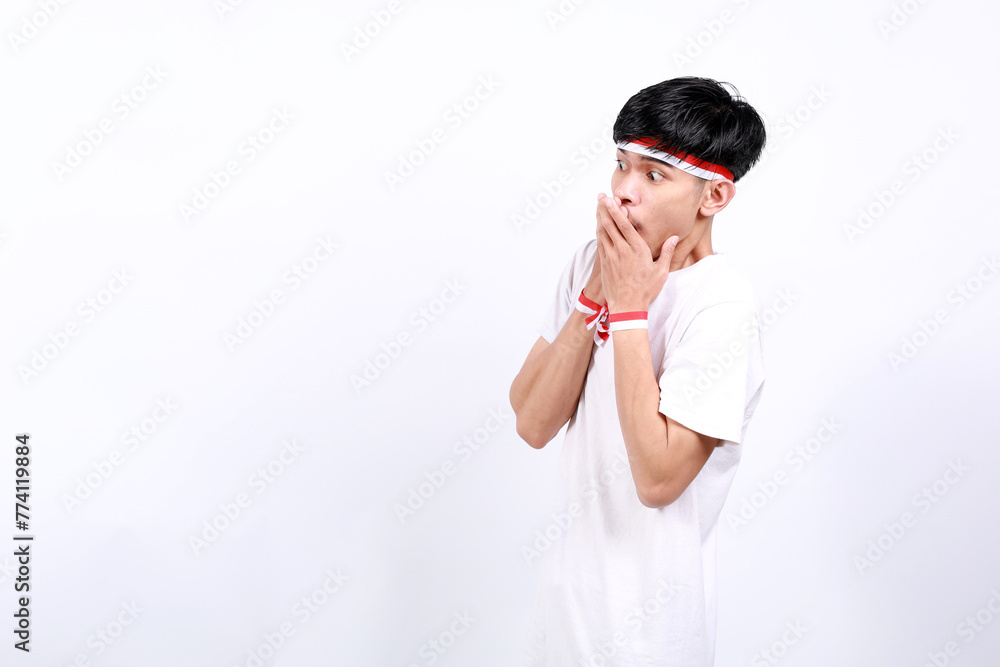 Shocked Young asian boy with red white ribbon celebrating Indonesia independence day while covering mouth and looking sideways Shocked Young asian boy with red white ribbon celebrating Indonesia independence day while covering mouth and looking sideways