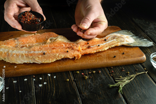 Cooking fish steak before grilling. The chef hand adds dry aromatic spices to fatty raw fish.