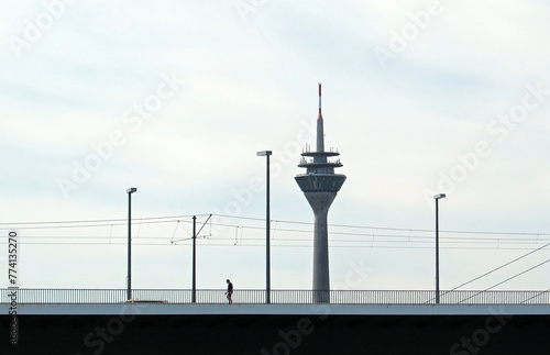 Lonely person walking on the Rhine bridge with the Rhine Tower at the background.	
