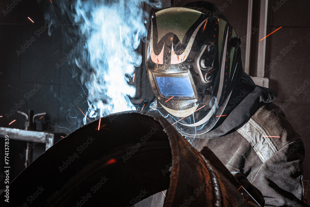 Fototapeta premium In a protective mask, a welder skillfully operates an arc welding machine, producing a dazzling display of sparks while expertly fusing metal together.