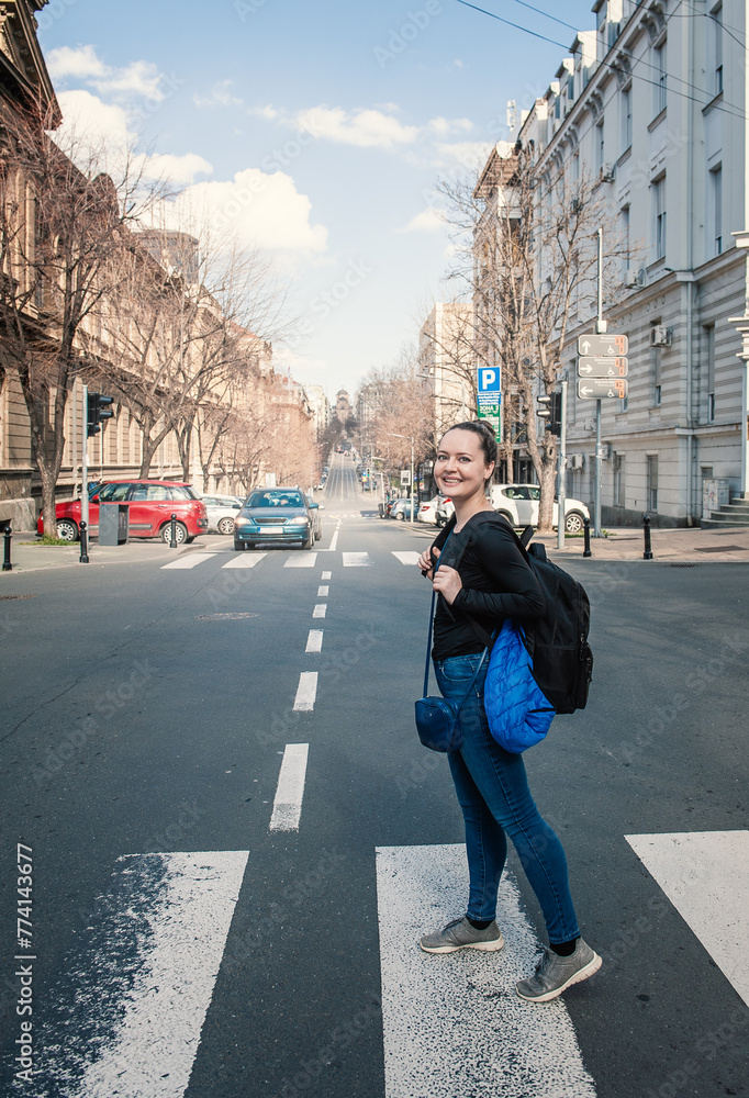 Beautiful smiling tourist woman with backpack standing on the crosswalk in the Belgrade city, Serbia