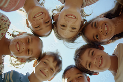 Group of happy kids hugging, looking down at camera and smiling. Low angle, view from below