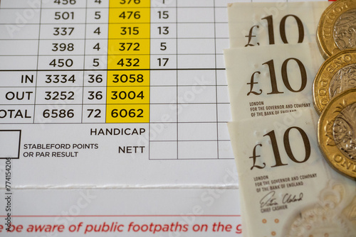 Close-up photograph of a Golf Course scorecard with cash in the form of ten pound notes and pound coins lying on the top of the score card. photo