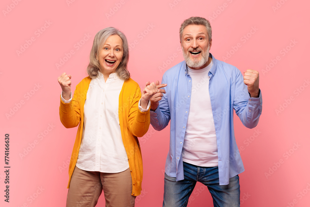 Excited mature spouses celebrating with yes gestures over pink backdrop Excited mature spouses celebrating with yes gestures over pink backdrop