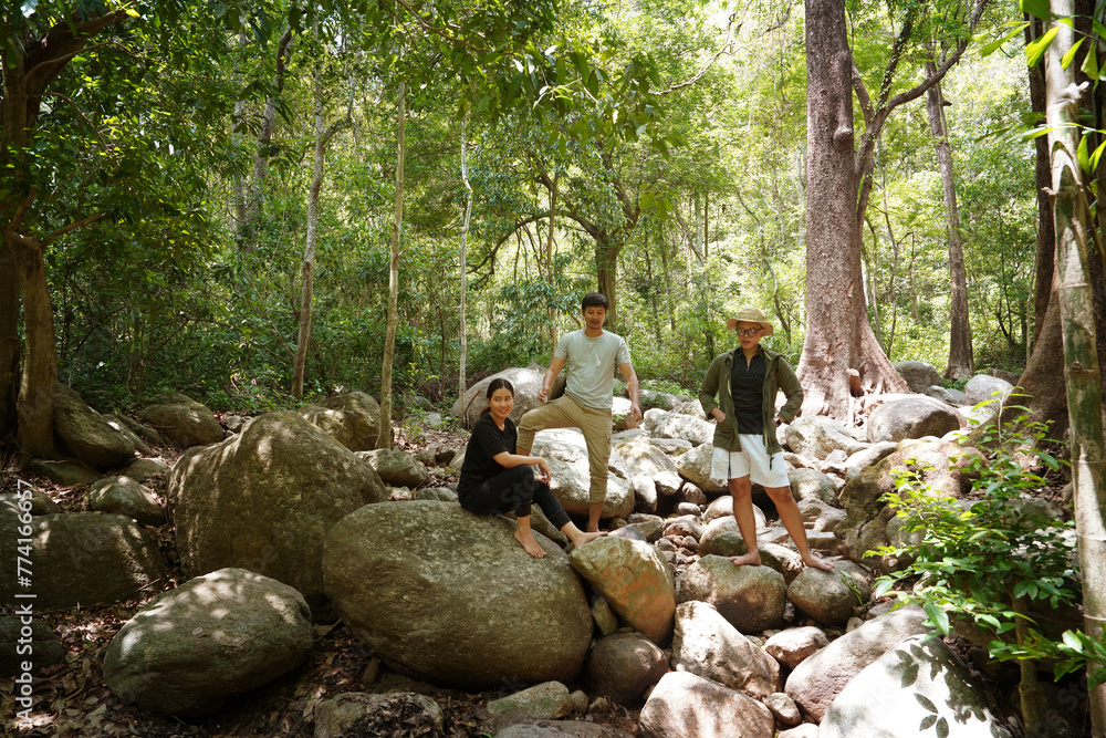 Group of three friends, one woman and two Asian men, hiking and sitting, camping, picnicking in the forest, having a stream and waterfall, relaxing during the weekend.Friendship and lifestyle