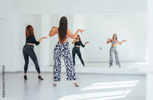 Graceful dancing women group doing elegant dance movements in white color spacious hall with big mirror wall.People's expressions during dancing, beauty of woman's body, active lifestyle concept image