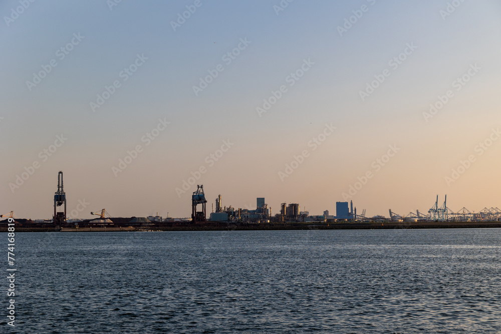 Ships float across the North Sea. Windmills in the background. Sea port in the Netherlands. A lot of cranes for loading goods. Different ships and barges.