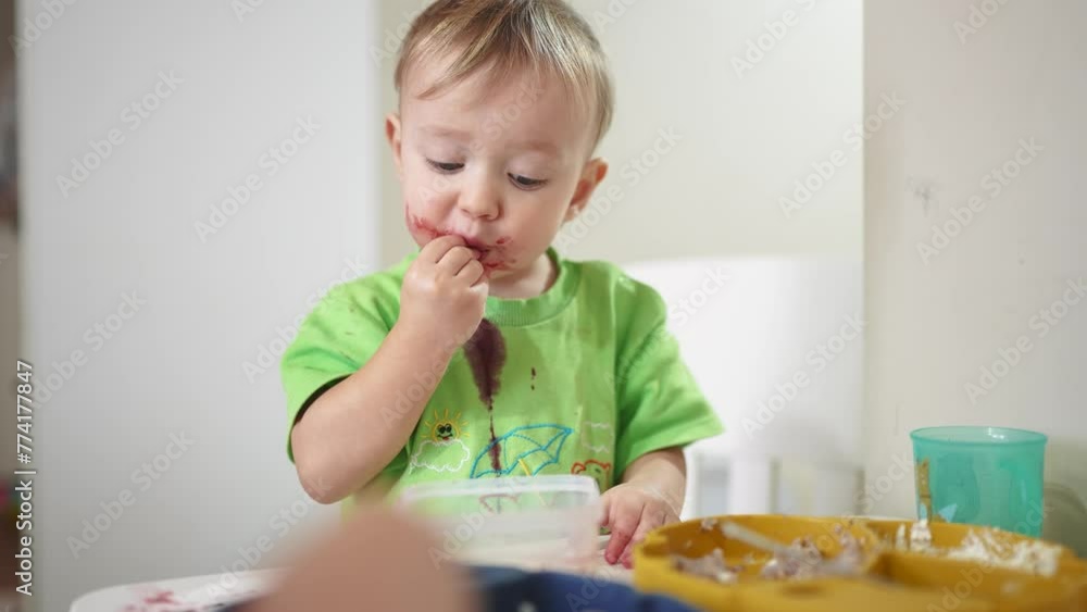 grimy baby eats at the table. baby learns to eat develops fine motor skills gets his face dirty. happy family kid lifestyle dream concept. baby blond son eats dirty grimy baby eats at the table. baby learns to eat develops fine motor skills gets his face dirty. happy family kid lifestyle dream concept. baby blond son eats dirty