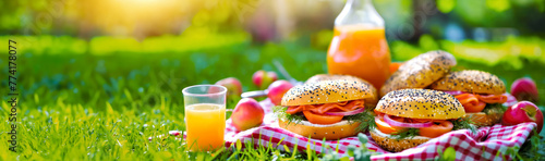 Summer picnic spread with fresh bagels and orange juice amidst a lush green background. banner