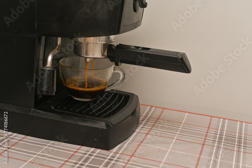 A coffee maker fills a glass cup with fragrant coffee photo