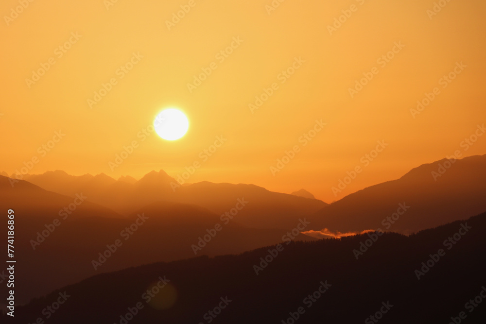 early morning sun rising over a hazy mountain range in an orange sky