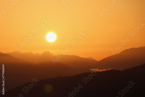 early morning sun rising over a hazy mountain range in an orange sky