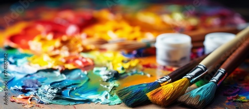 Palette with various colorful paint tubes and an assortment of different paintbrushes placed on a wooden table