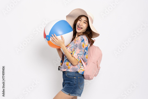 Happy Young Asian traveler woman wearing floral dress smiling with backpack and holding beach ball isolated on white background, Tourist in summer and holidays vacation concept