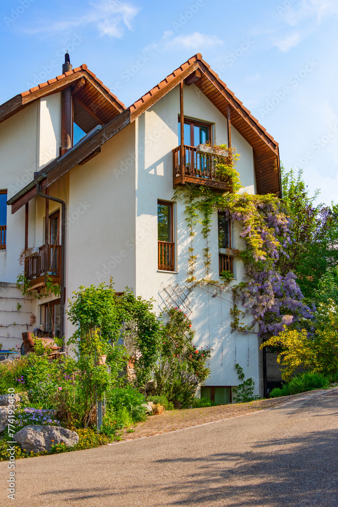 Fototapeta premium The facade of a traditional house of a small Swiss town, the house is decorated with a wooden roof and balconies, the stone walls are covered with flowers