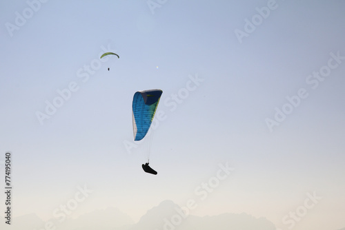  two paragliders in the air with a monochrome background of a hazy mountain range in different shades of grey