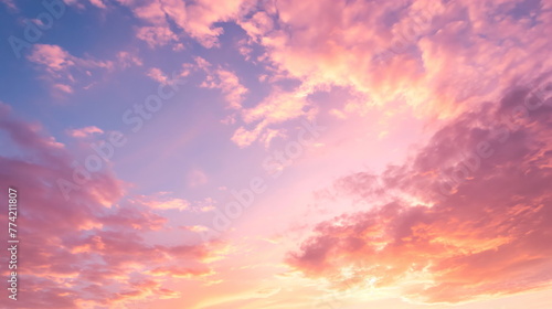 Pink and orange clouds illuminated by the setting sun against a soft blue sky photo
