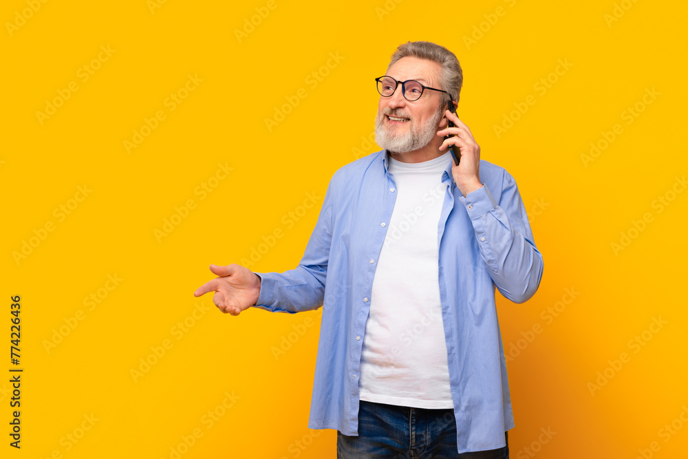 Cheerful senior man talking on cell phone on yellow background Cheerful senior man talking on cell phone on yellow background