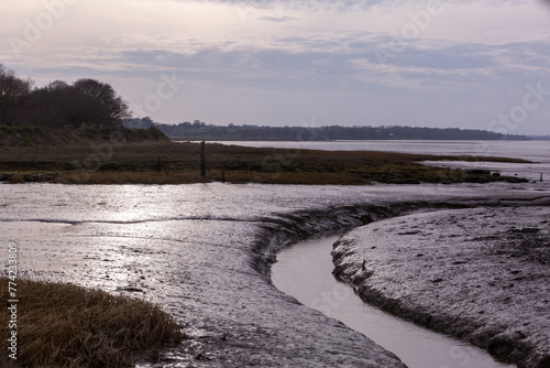 Winding Stream heading to the sea in muddy uk river Stour at Wrabness beach as the sun begins to set on a cloudy day photo