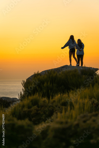 Two unrecognizable teenage girls enjoying the sunset on the seashore during vacation photo