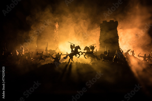 Medieval battle scene with cavalry and infantry. Silhouettes of figures as separate objects, fight between warriors on dark toned foggy background. Night scene. photo