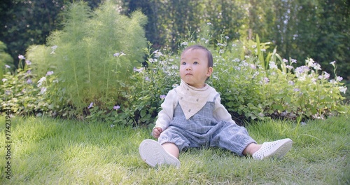 A baby child toddler is sitting on the grass and holding a leaf. The baby girl is smiling and looking at the camera. The scene is peaceful and calm, with the baby enjoying the outdoors