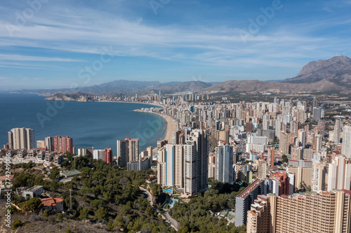 Aerial drone photo of the town of Benidorm in Spain in the summer time showing high rise apartments and building along side the Levante Beach and mountings in the background.