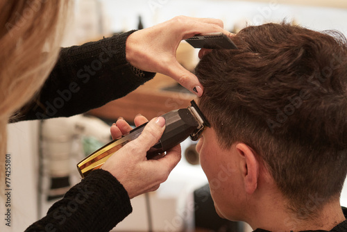 An hairdresser cuts a woman's hair with an electric razor in an hair salon