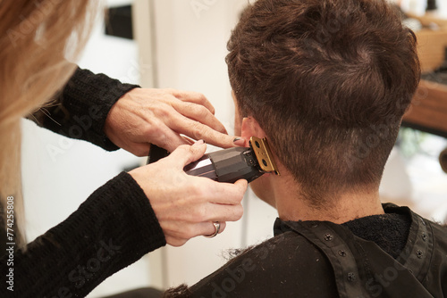 An hairdresser cuts a woman's nape's hair behind the ear with an electric razor in an hair salon