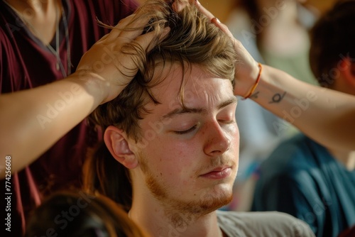 A young man relaxes with his eyes closed while receiving a head massage in a workshop setting.
