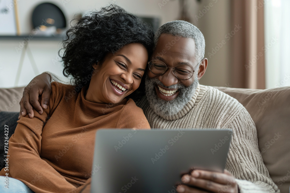 laughing couple on her couch looking at her laptop in living bright environment at home