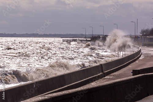 Rough high tide or spring tide on Dovercourt beach, Harwich with larges waves hitting against the sea wall completely covering the sandy beaches  photo