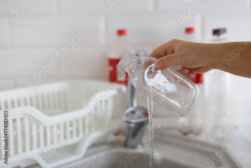 A woman's hand washes a plastic bottle in a white kitchen. A woman sorts plastic and collects it to send to a recycling service. The concept of environmental friendliness, plastic recycling.