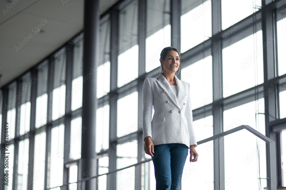 Good-looking woman in white jacket and jeans in the office building Good-looking woman in white jacket and jeans in the office building